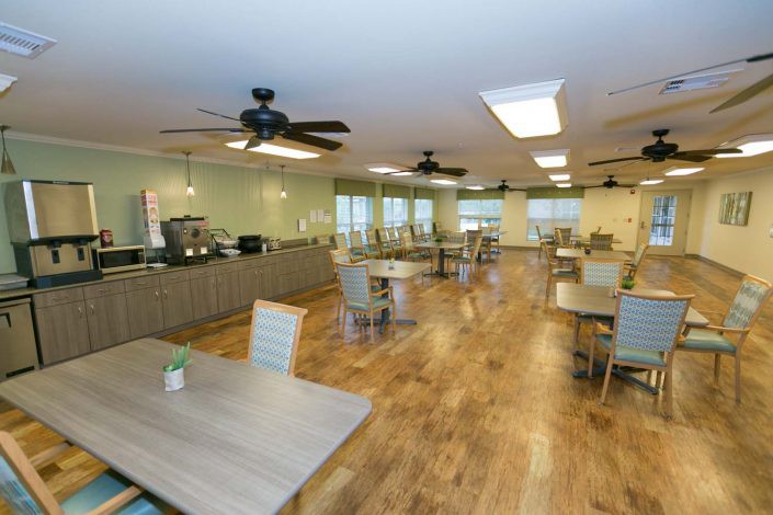 A spacious and well-lit dining area with wooden flooring, featuring several tables and chairs.
