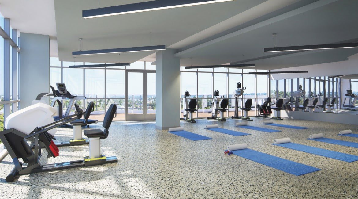 A modern gym with exercise equipment and yoga mats positioned in front of large windows.