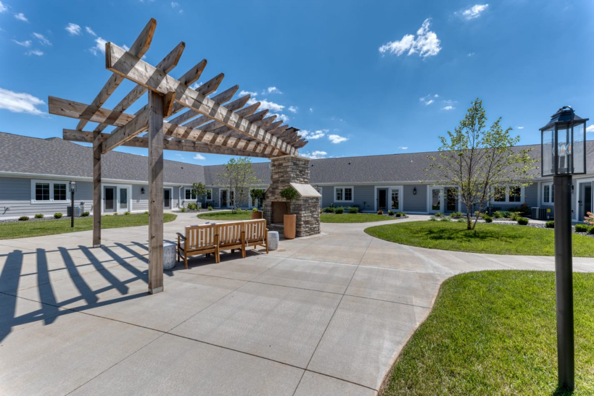 A serene courtyard featuring a pergola with benches and a paved walkway under a clear blue sky.