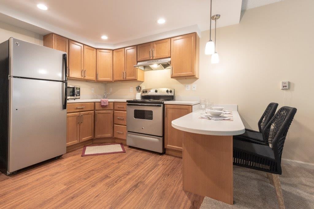 A modern kitchen featuring wood cabinets, stainless steel appliances, and a cozy countertop with bar stools.