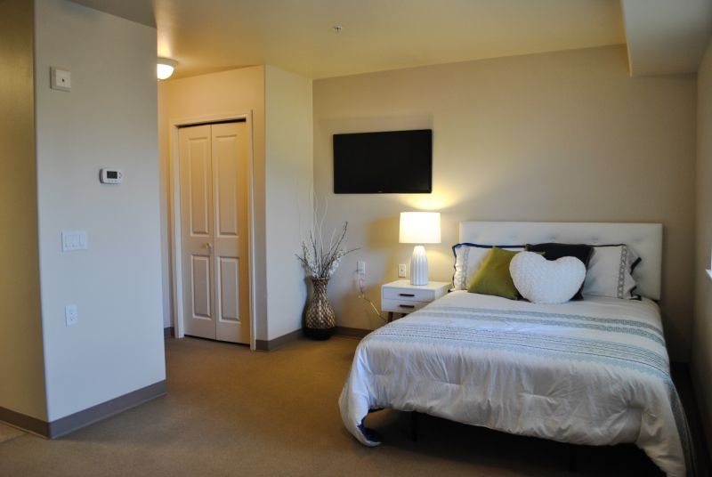 A modern bedroom with a neatly made bed, heart-shaped pillow, and a bedside lamp.
