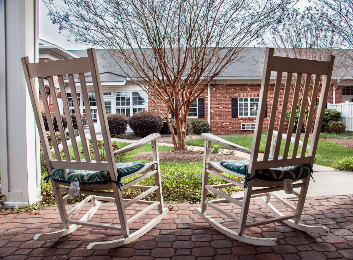 Two rocking chairs facing a peaceful garden and brick house.