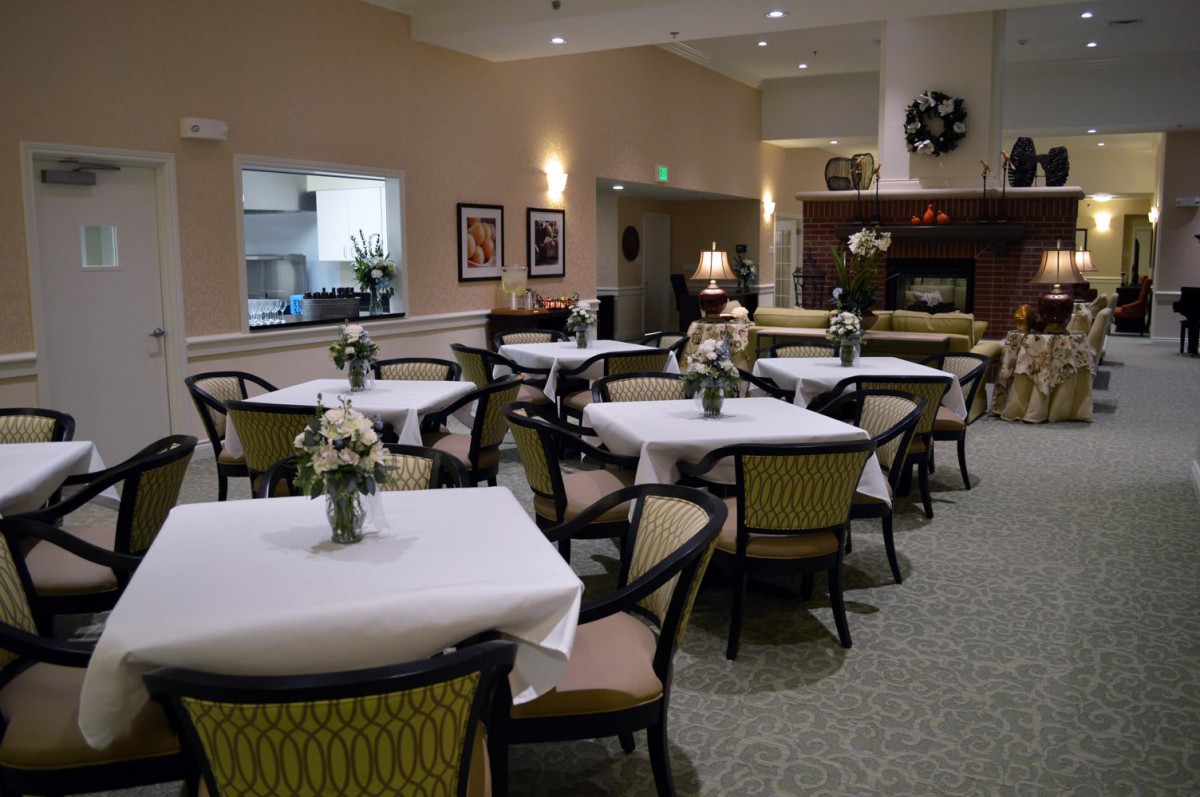 A well-decorated dining room with multiple tables and chairs, featuring floral centerpieces and soft lighting.