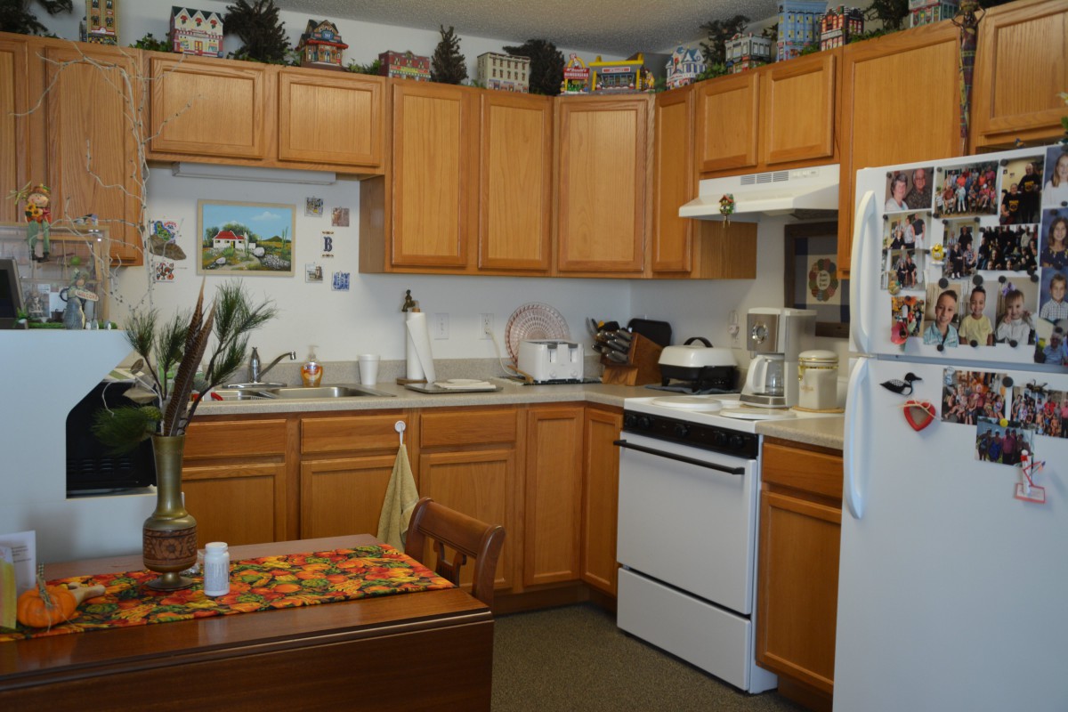 A cozy kitchen featuring wooden cabinets, a stove, refrigerator, and countertop with various appliances and decorations.