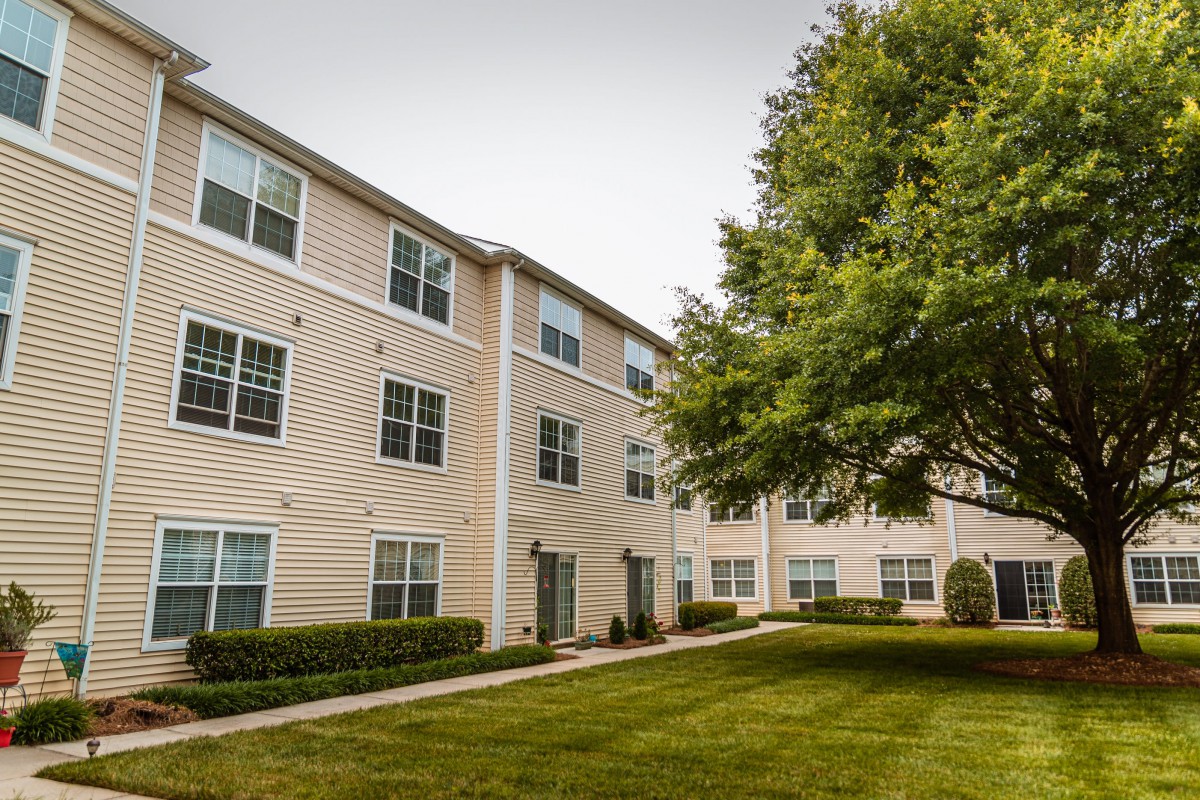 A view of a residential apartment building with a well-maintained lawn and trees.