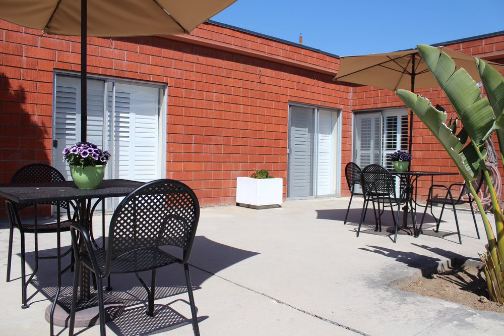 A sunny outdoor patio with tables, chairs, and large umbrellas next to a brick building.