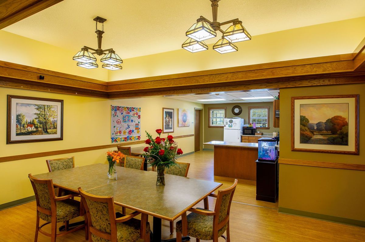 A cozy dining room with a wooden table, chairs, and decorative lighting, featuring a kitchen area in the background.