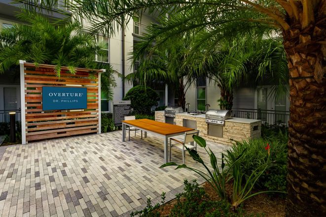 A modern outdoor barbecue area with grills, tables, and lush tropical greenery.