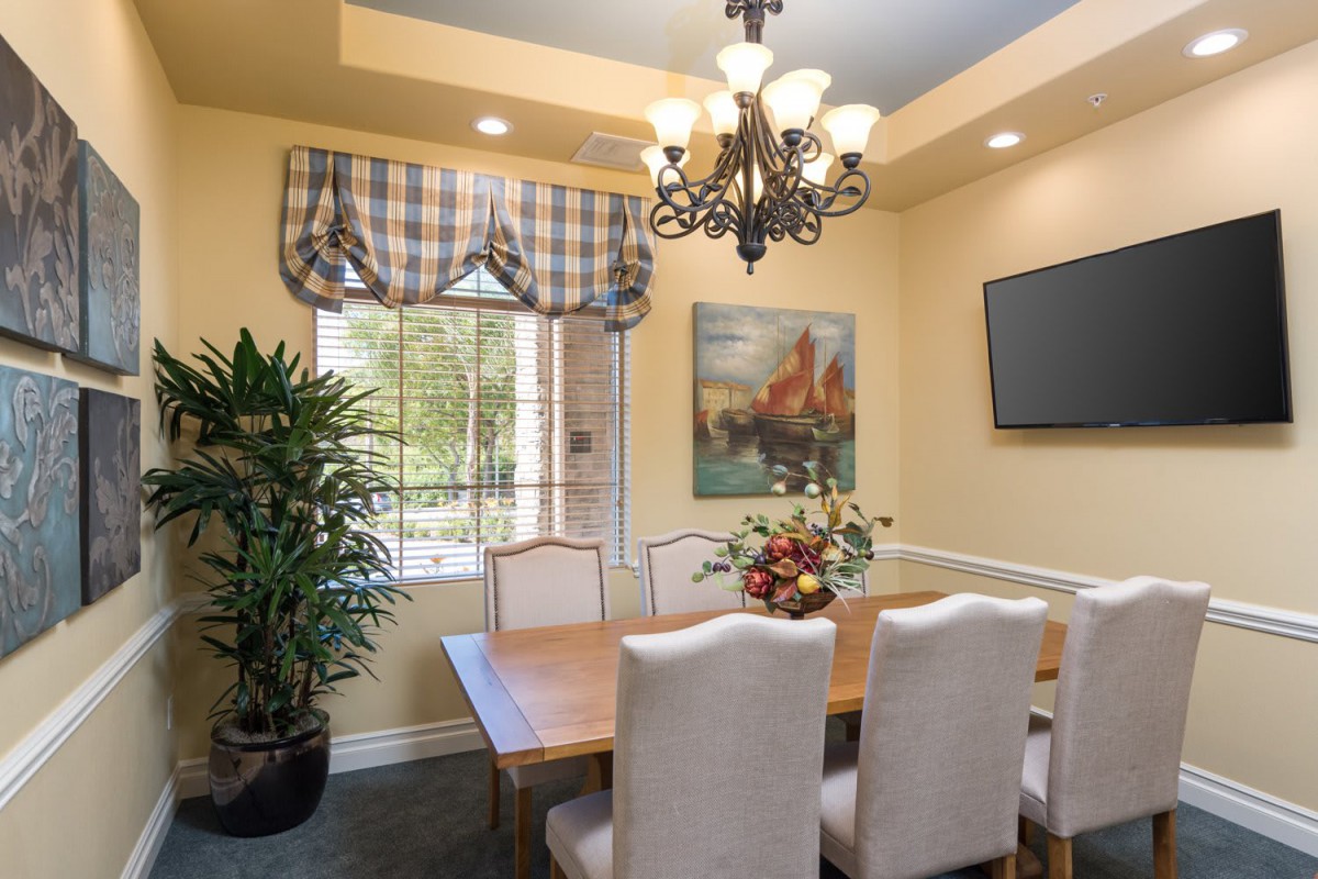 A cozy dining room with elegant furnishings, featuring a chandelier, a large window with plaid curtains, and a decorative plant.