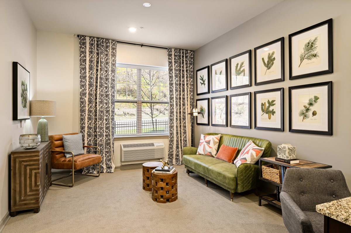 A cozy living room featuring a green sofa, decorative wall art, and patterned curtains.