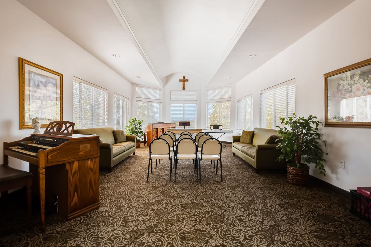 A spacious, well-lit room with sofas and a cross on the wall, suggesting a chapel-like setting.