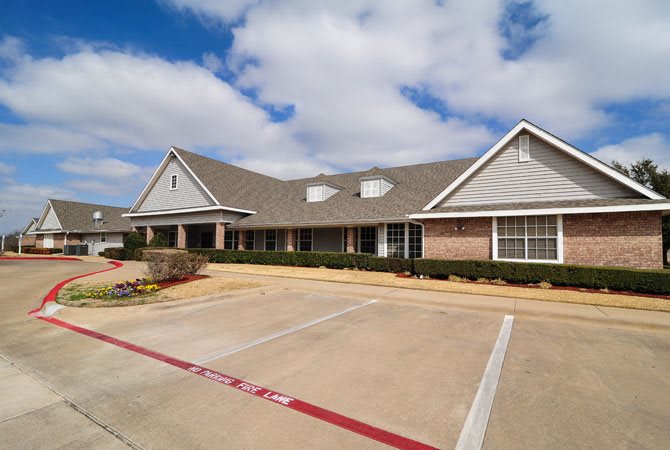 A suburban residential building with a large driveway and parking lot under a partly cloudy sky.