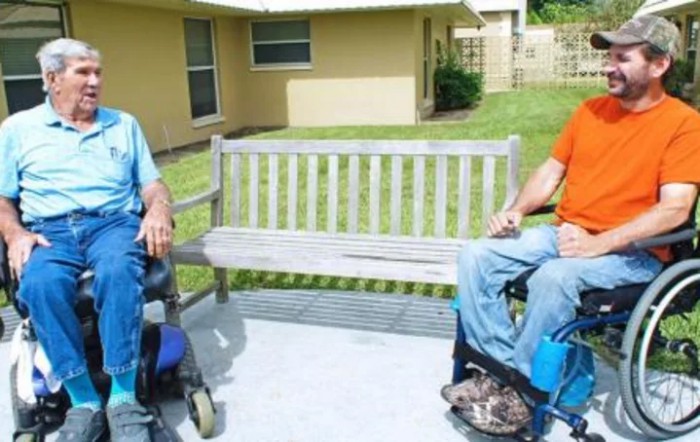 Two people in wheelchairs having a conversation outdoors near a bench.