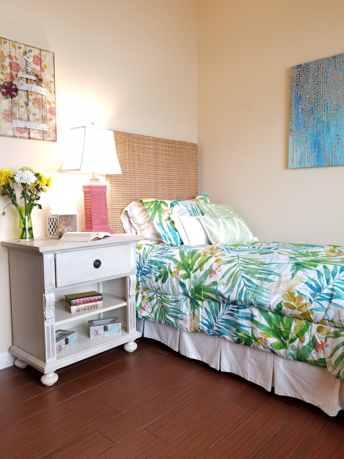 A cozy bedroom with a colorful bedspread and a white nightstand adorned with flowers and a lamp.
