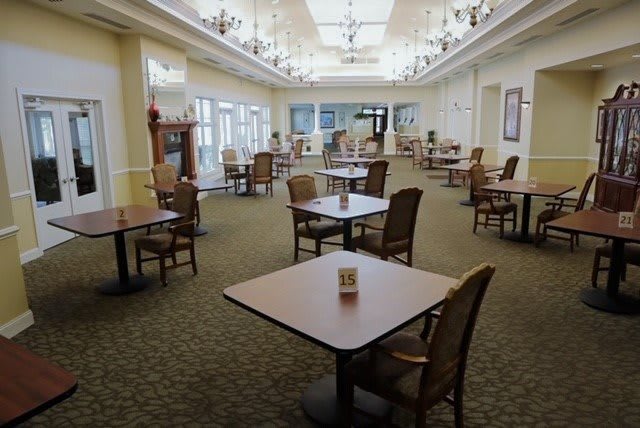 An empty dining area with neatly arranged tables and chairs, featuring chandeliers and a bright interior.
