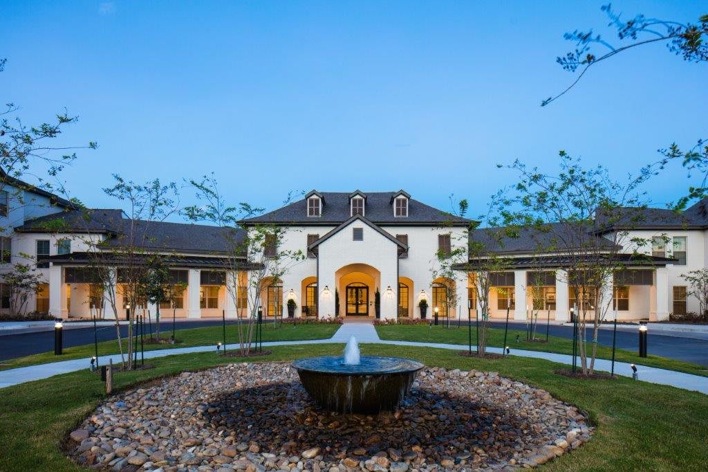 A large, elegant building with a central fountain and landscaped surroundings during the evening.