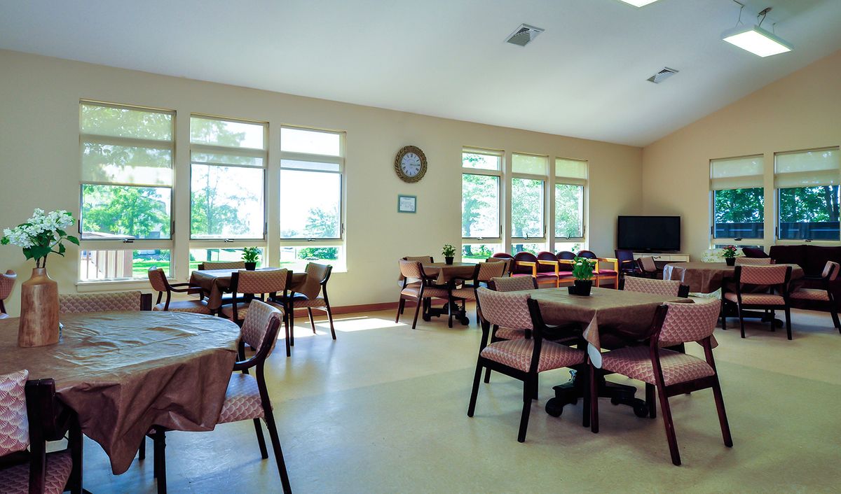 A spacious dining area with multiple tables and chairs, well-lit by natural light through large windows.