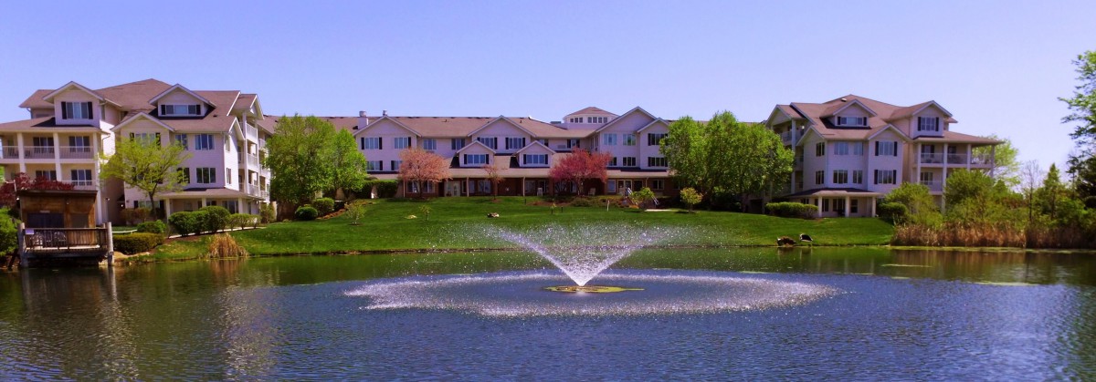 A scenic view of a building with a fountain in the foreground, surrounded by lush greenery.
