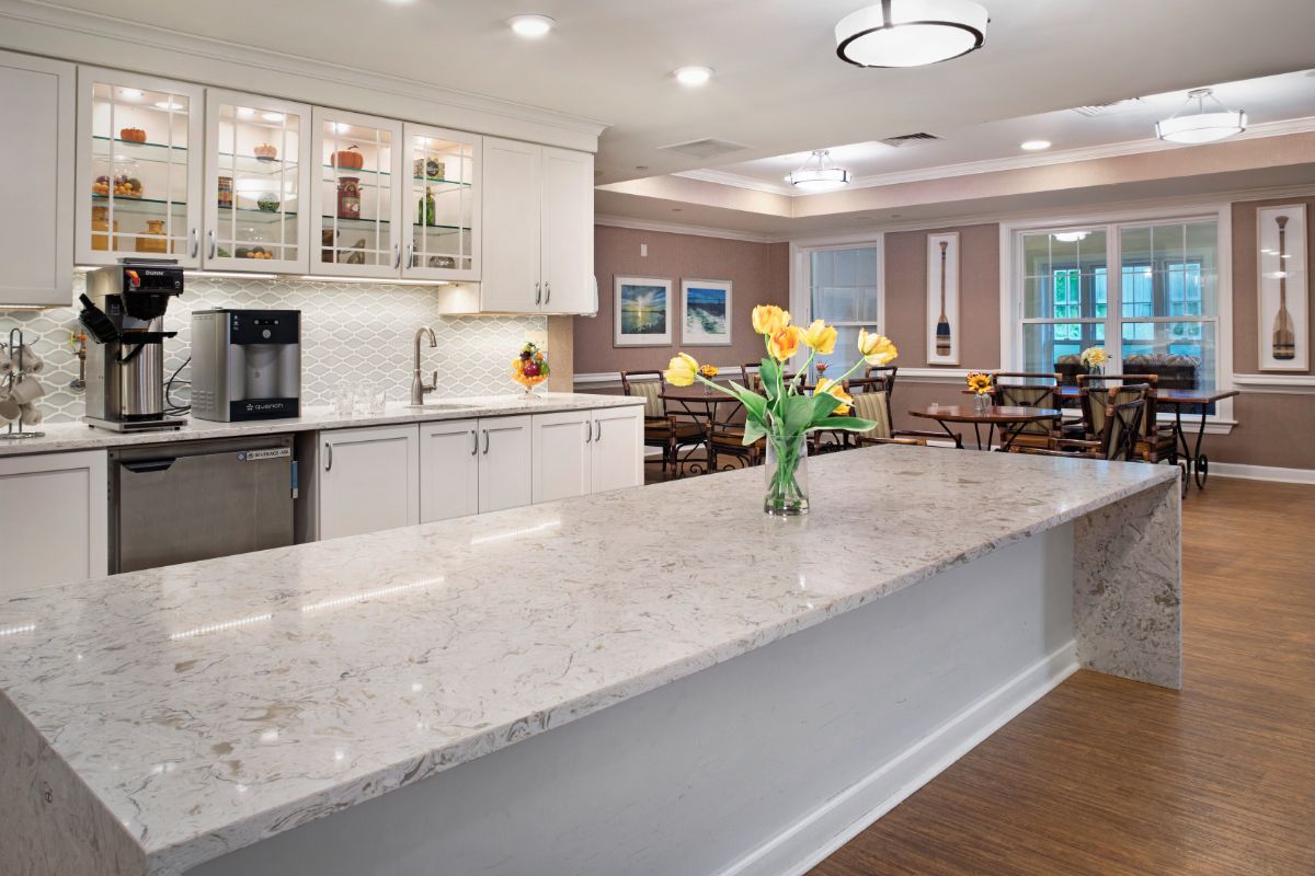 A modern kitchen with a marble countertop, flowers, and an adjacent dining area.