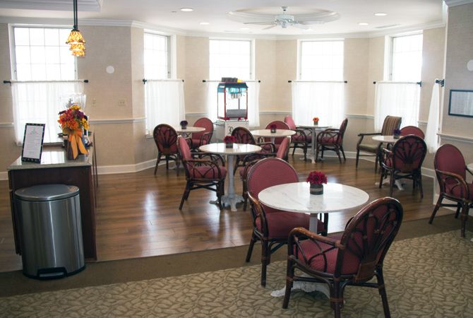 A cozy cafe interior with several tables and chairs, wooden flooring, and large windows providing natural light.