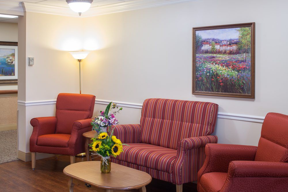 A cozy living room with red upholstered furniture, a wooden table with a vase of flowers, and a painting on the wall.