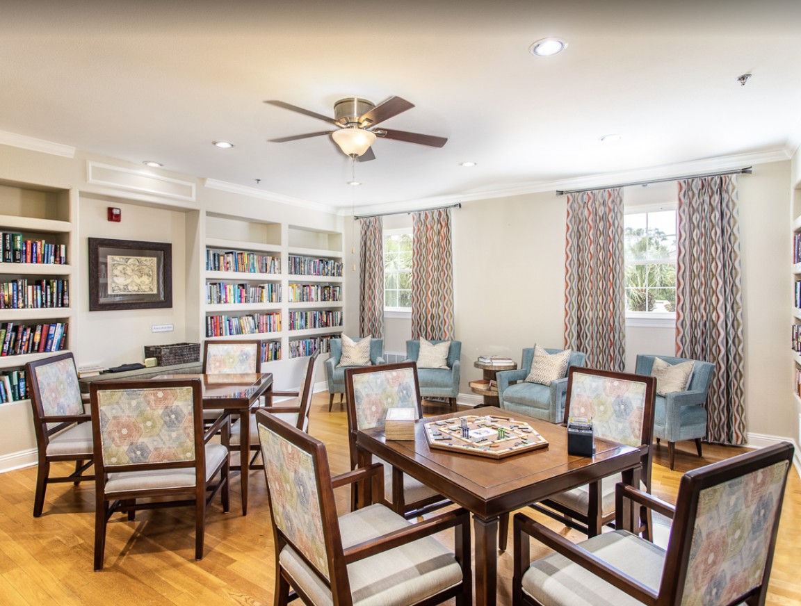 A cozy library room with wooden furniture, a table for board games, and bookshelves filled with books.