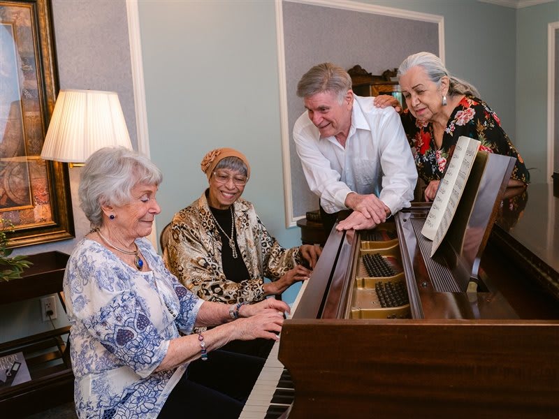 A group of seniors enjoying a musical session around a piano.