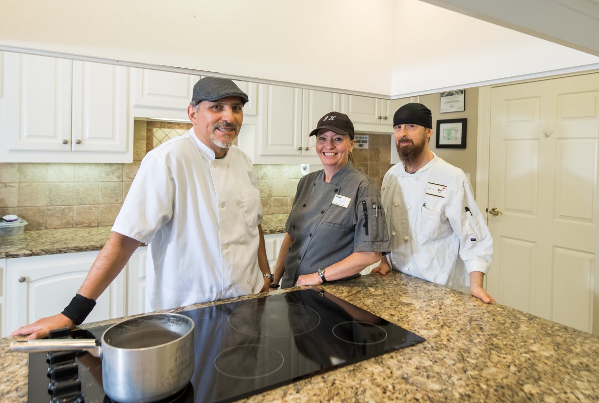 A group of three chefs standing together in a professional kitchen setting.