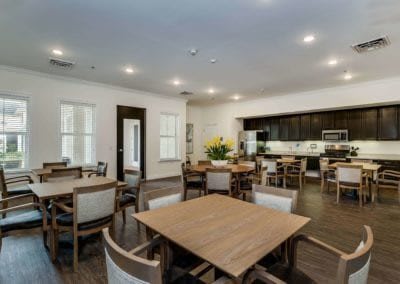 A modern dining area with wooden tables and chairs, adjacent to a kitchen.