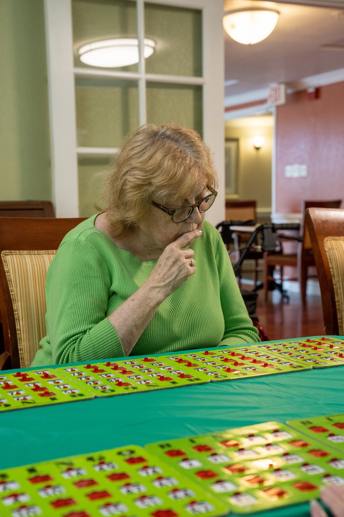 A thoughtful woman wearing a green shirt is seated at a table indoors.
