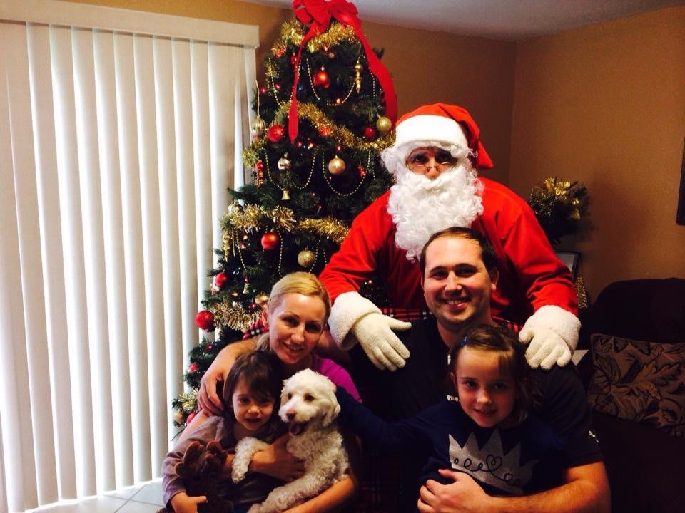 A family poses with Santa Claus in front of a decorated Christmas tree, along with their dog.