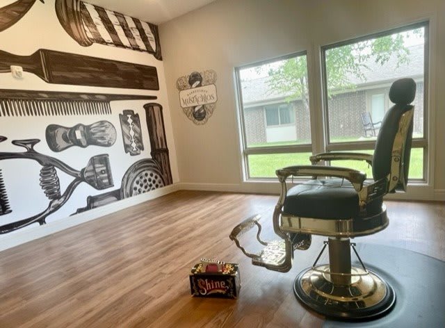 Stylish barbershop interior with a classic barber chair, artistic wall decor, and natural light from large windows.
