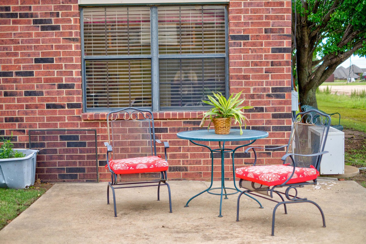 A cozy patio setup with a small round table, red-cushioned chairs, and a potted plant against a brick wall.