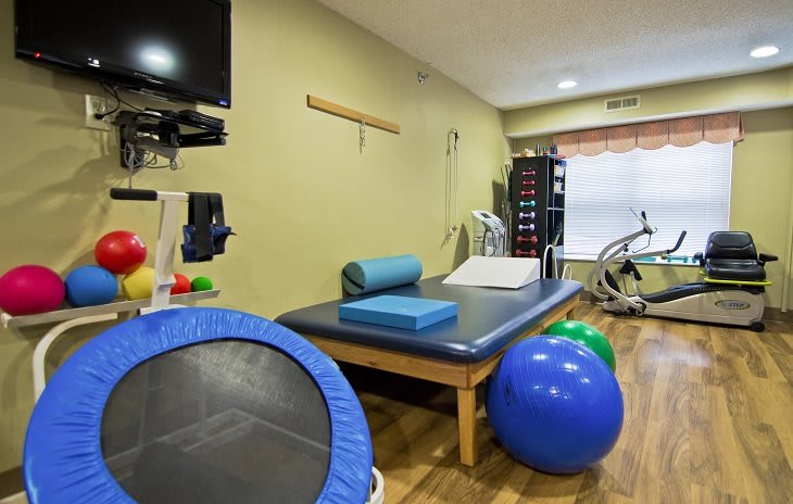 A physical therapy room equipped with exercise equipment, including a trampoline and medicine balls.