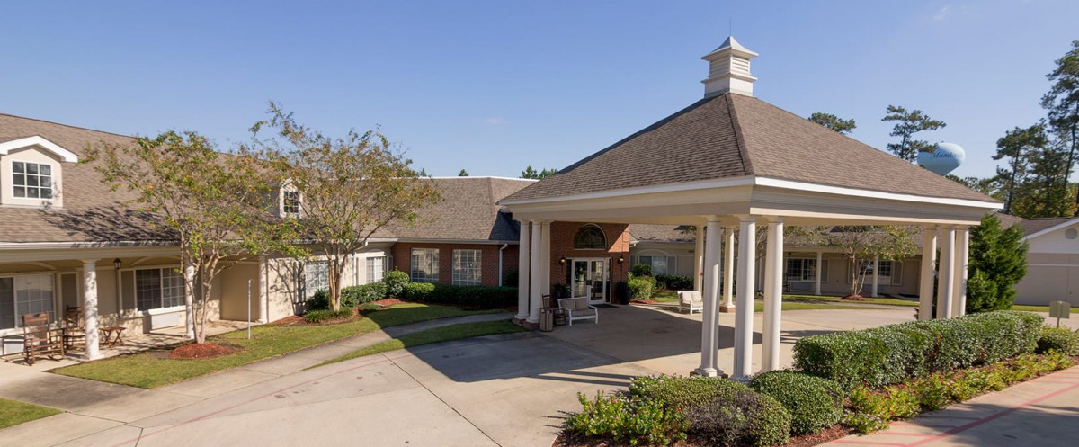 A front view of a building entrance with columns and surrounding landscaping on a clear day.
