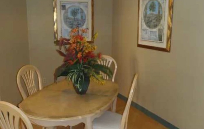 A dining area featuring a wooden table with a vibrant flower arrangement, surrounded by chairs and decorated with framed artwork on the walls.
