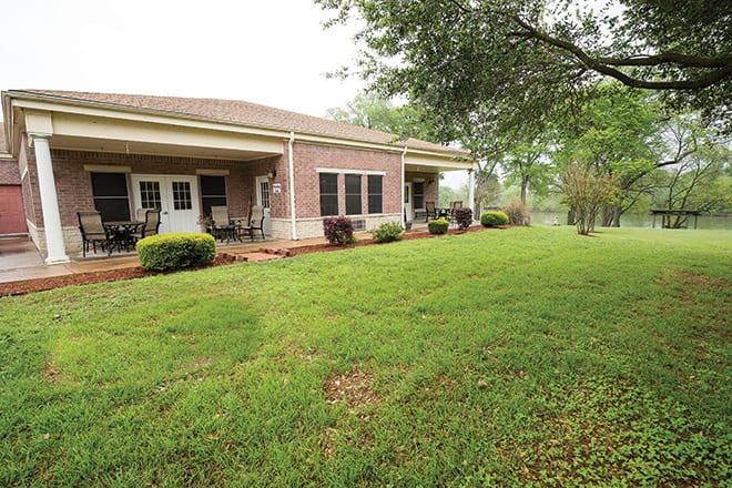 A view of a brick house with a well-maintained backyard and patio area.