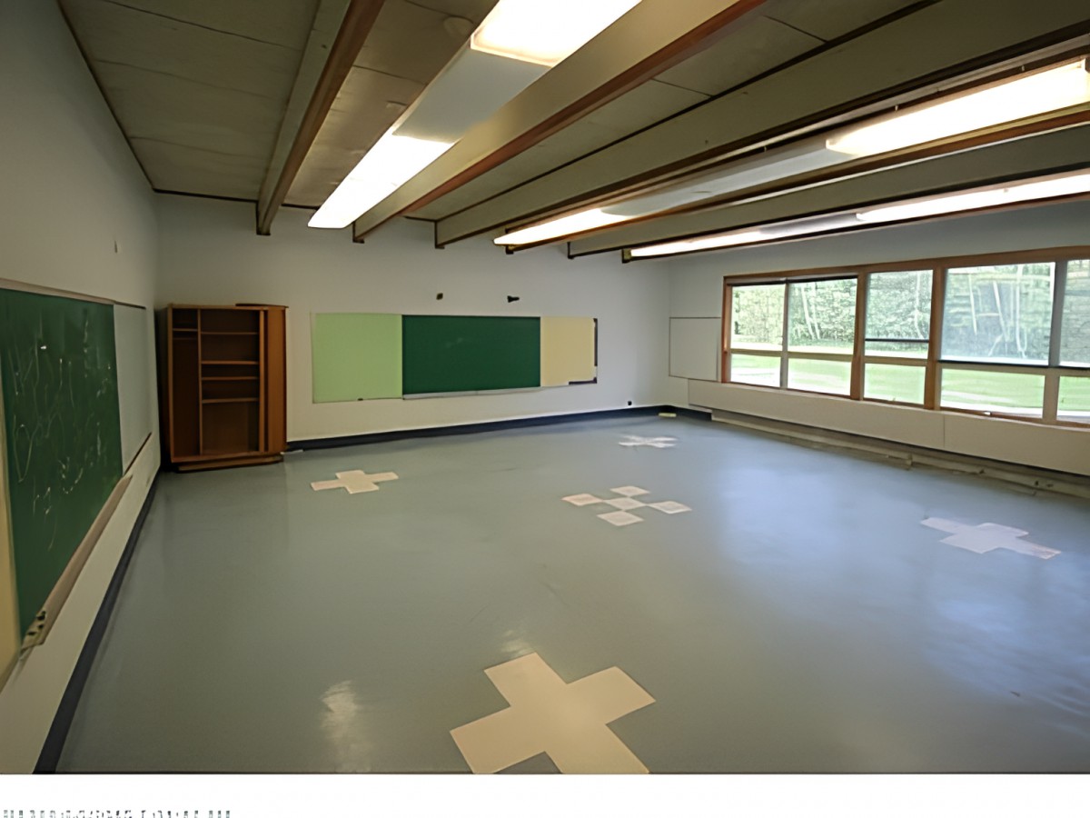 An empty classroom with a chalkboard, windows, and tiled floor.