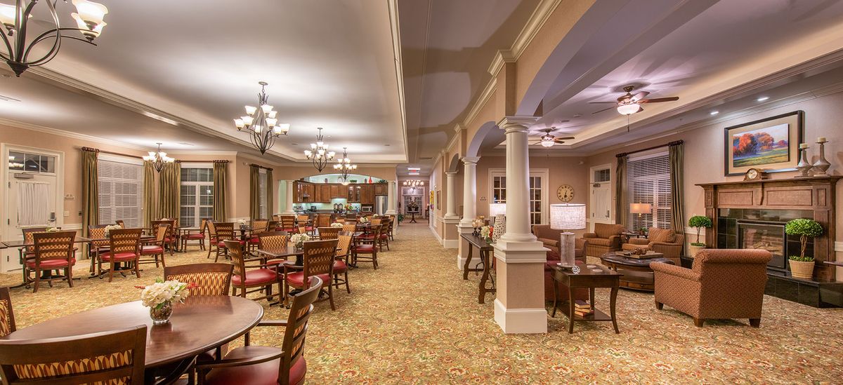 An elegant dining area with chandeliers, tables, and columns.