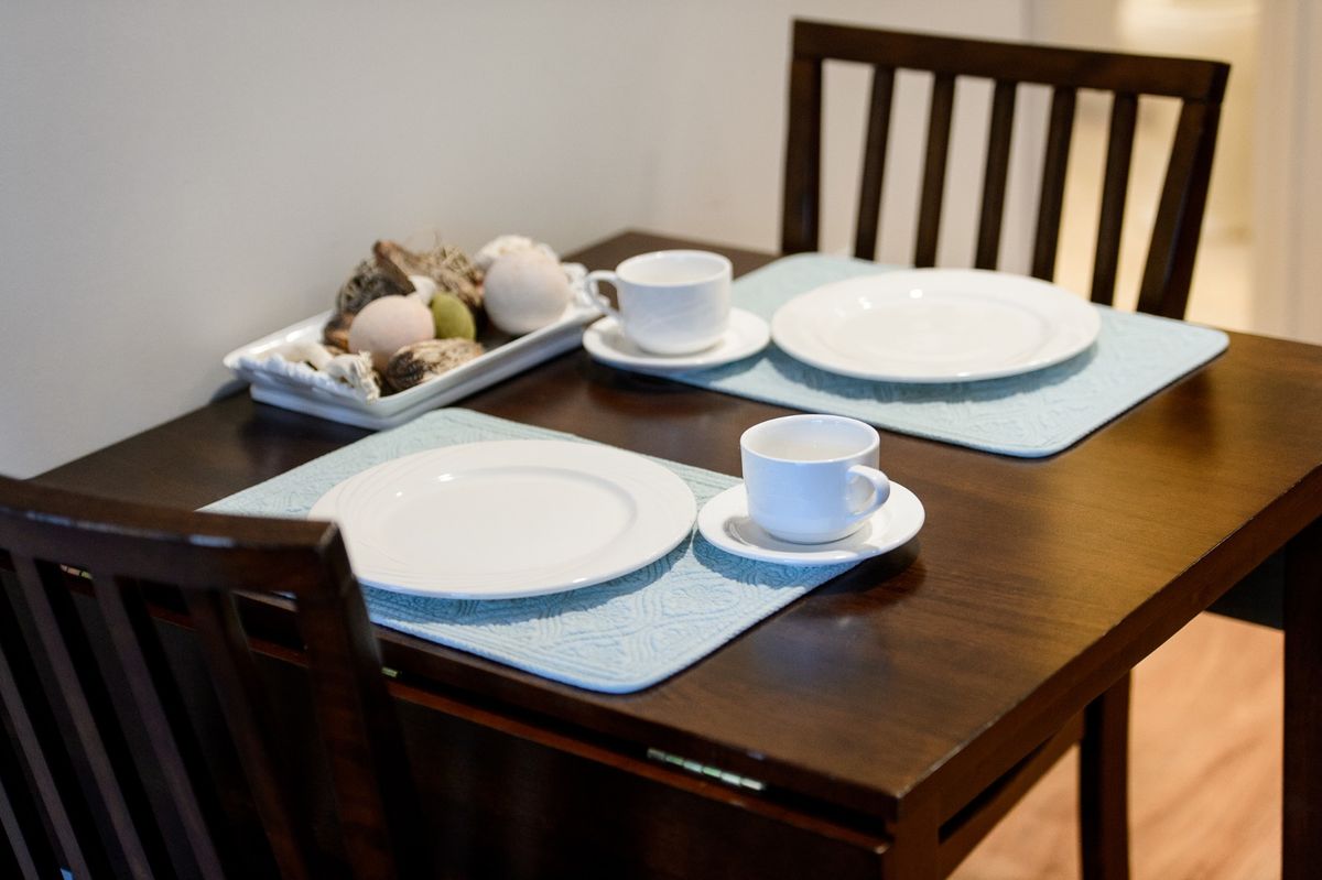 A neatly set dining table with plates and cups on light blue placemats.