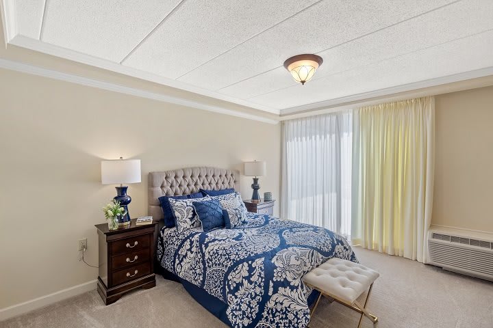 A well-decorated bedroom featuring a patterned bedspread, matching lamps on nightstands, and bright natural lighting.