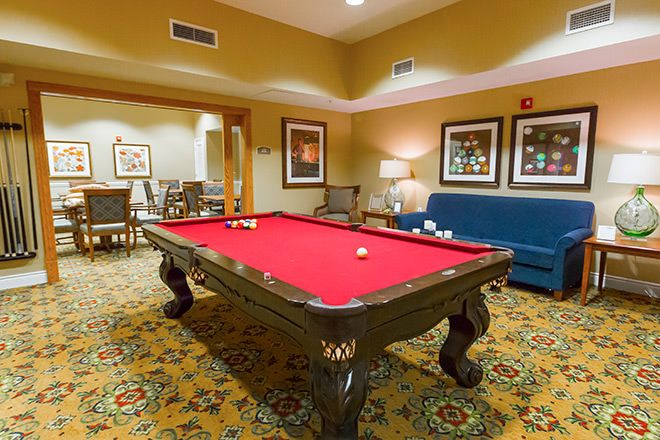 A cozy game room featuring a red felt pool table surrounded by furniture and artwork.