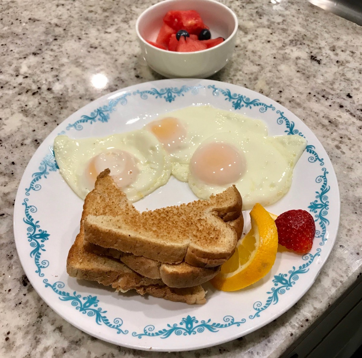 A breakfast plate with eggs, toast, and fruit, accompanied by a bowl of berries.