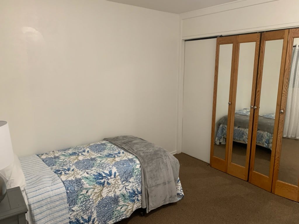 A minimalist bedroom featuring a single bed with floral bedding next to mirrored closet doors.