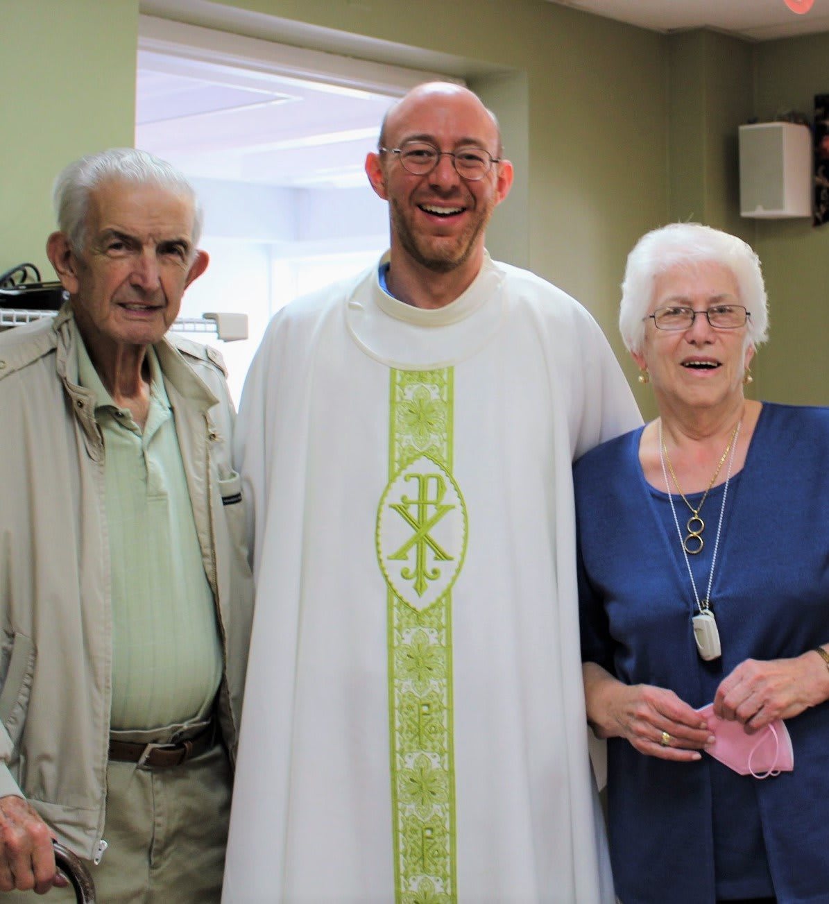 A group of three people, including a priest, smiling indoors.