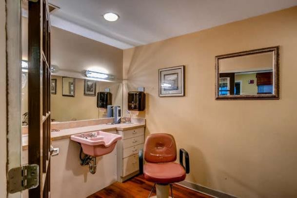 A well-lit bathroom with a pink sink, mirror, and a cushioned chair.