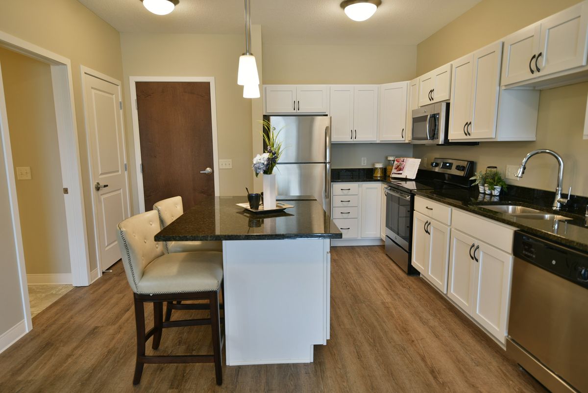 A modern kitchen featuring an island with bar stools, stainless steel appliances, and white cabinets.