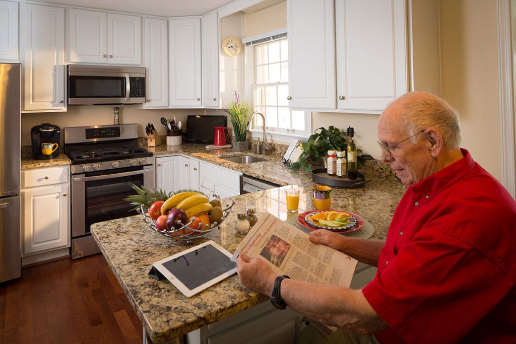 An elderly man reads a newspaper in a modern kitchen, surrounded by fresh fruit and technology.