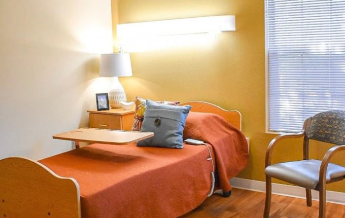 A cozy bedroom with a hospital bed featuring orange bedding, a bedside lamp, and wooden furniture.