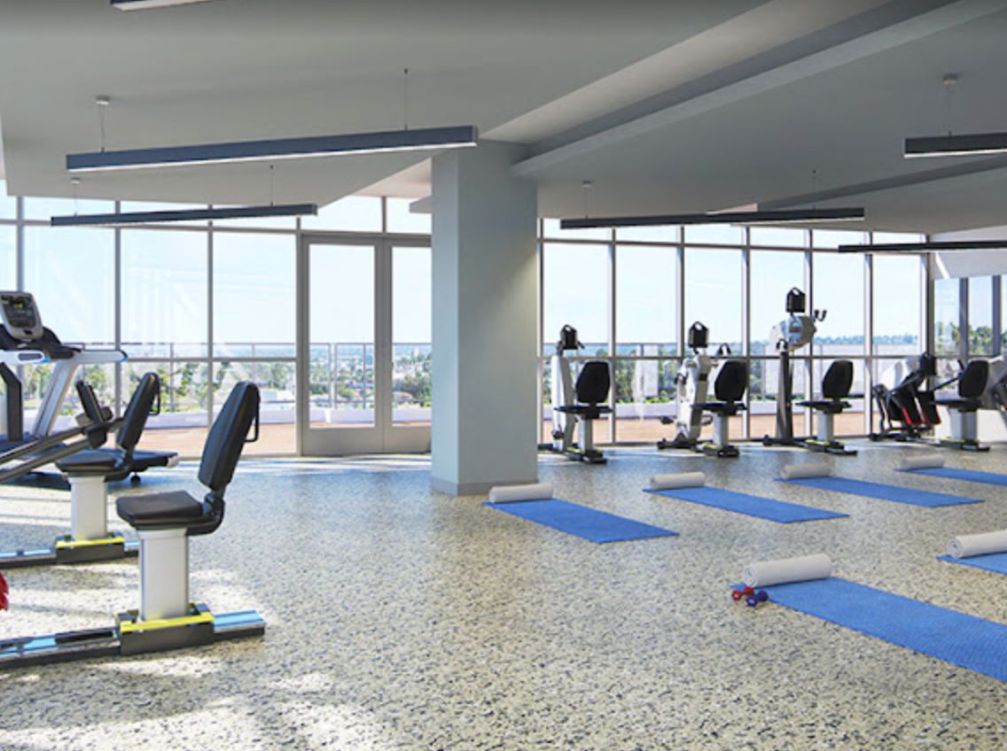 A spacious gym with exercise equipment, yoga mats, and large windows providing natural light.